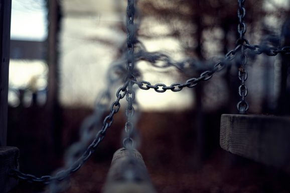 Verschnörkelte Kette im Vordergrund, unscharfer Hintergrund mit Bäumen.