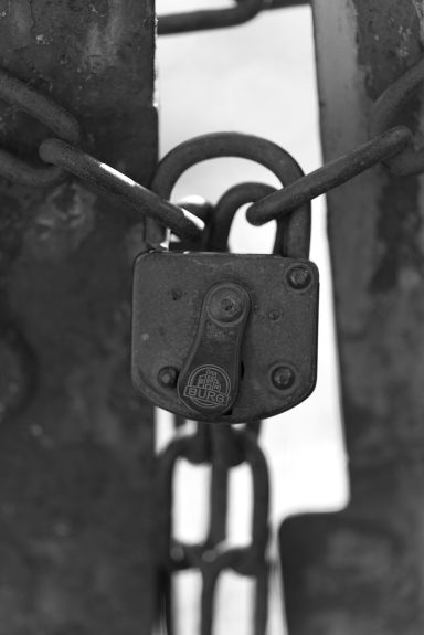 Ein schwarzes, rostiges Vorhängeschloss an einer Kette.