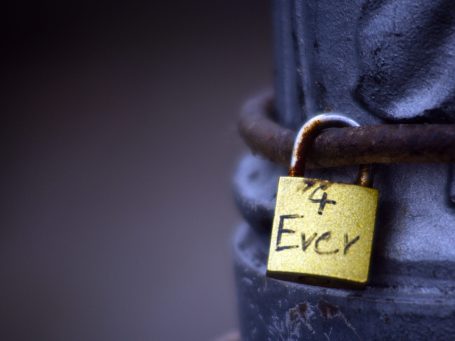 Gelber Vorhängeschloss mit der Aufschrift „4 Ever“ an einem Metallpfosten.