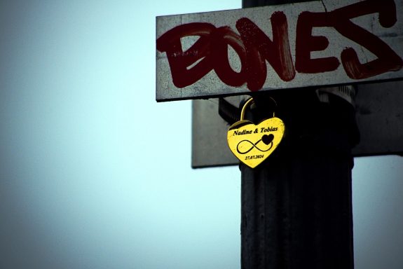 Gelbes Liebesschloss an einem Pfosten mit graffitiartigem Schriftzug "BONES".