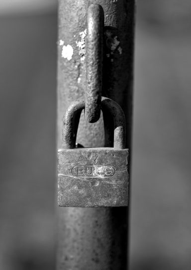 Ein rostiger Vorhängeschloss, der an einem Metallzaun befestigt ist.
