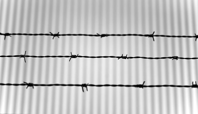 Drahtzaun mit Stacheldraht vor einer gestreiften Wand.