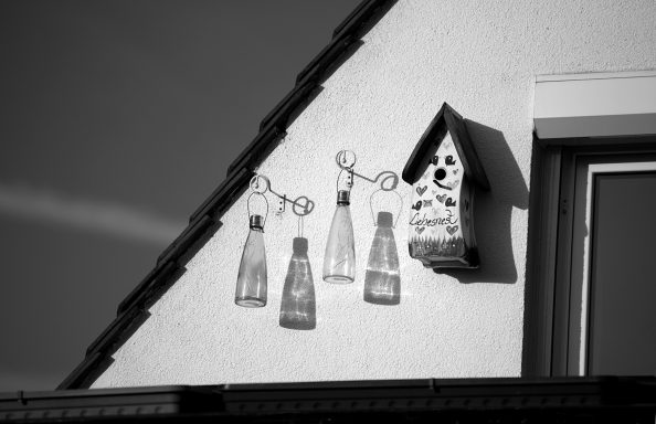 Balkon mit Vogelhaus und entleerten Flaschen, monochrome Darstellung.