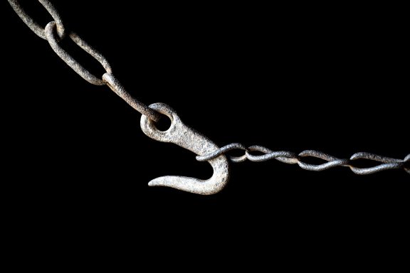 Verchromter Haken an einer Kette auf schwarzem Hintergrund.